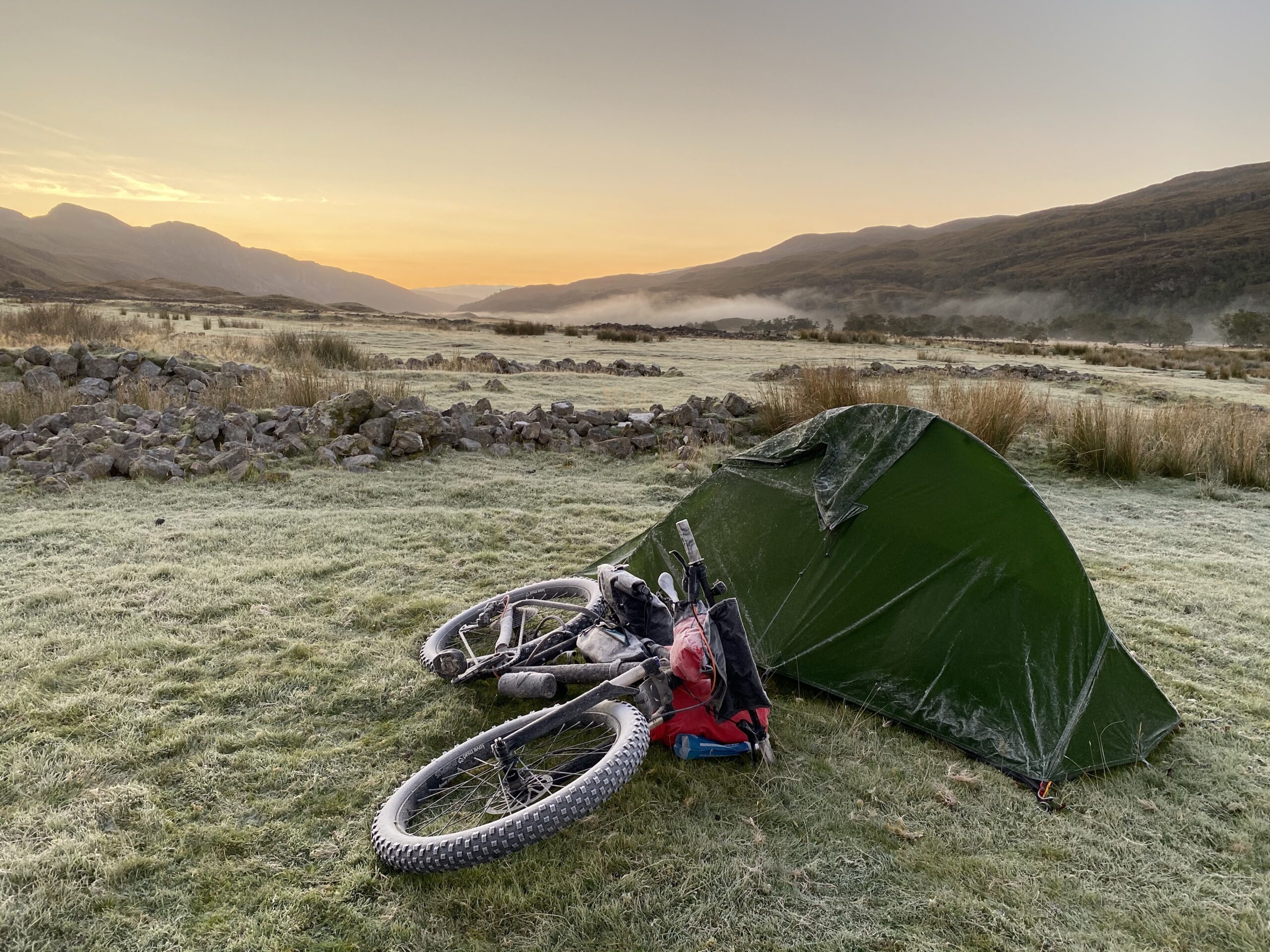 Frosty bike and tent with sunrise behind. 